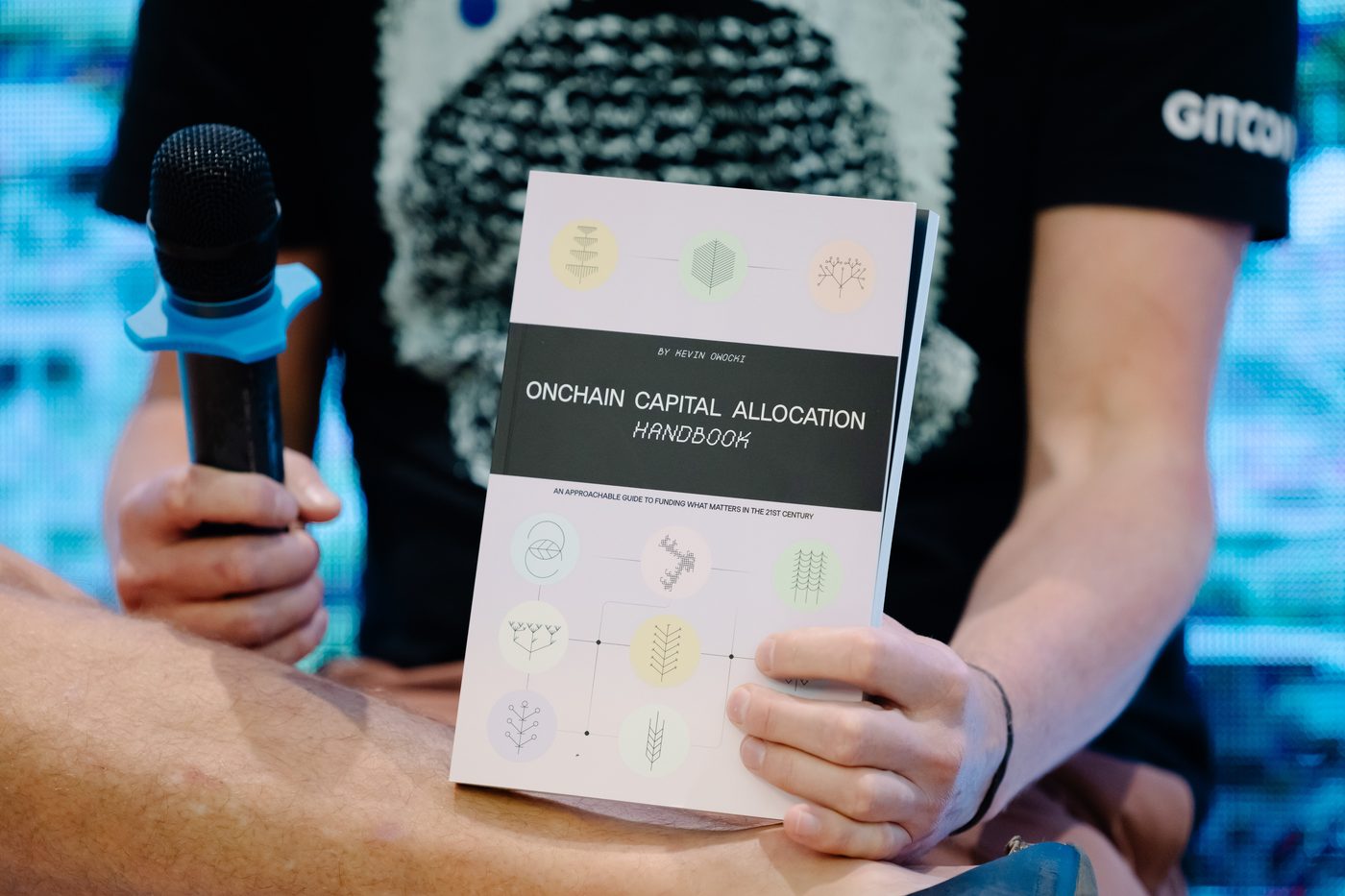 Kevin Owocki holding the Onchain Capital Allocation Handbook on stage